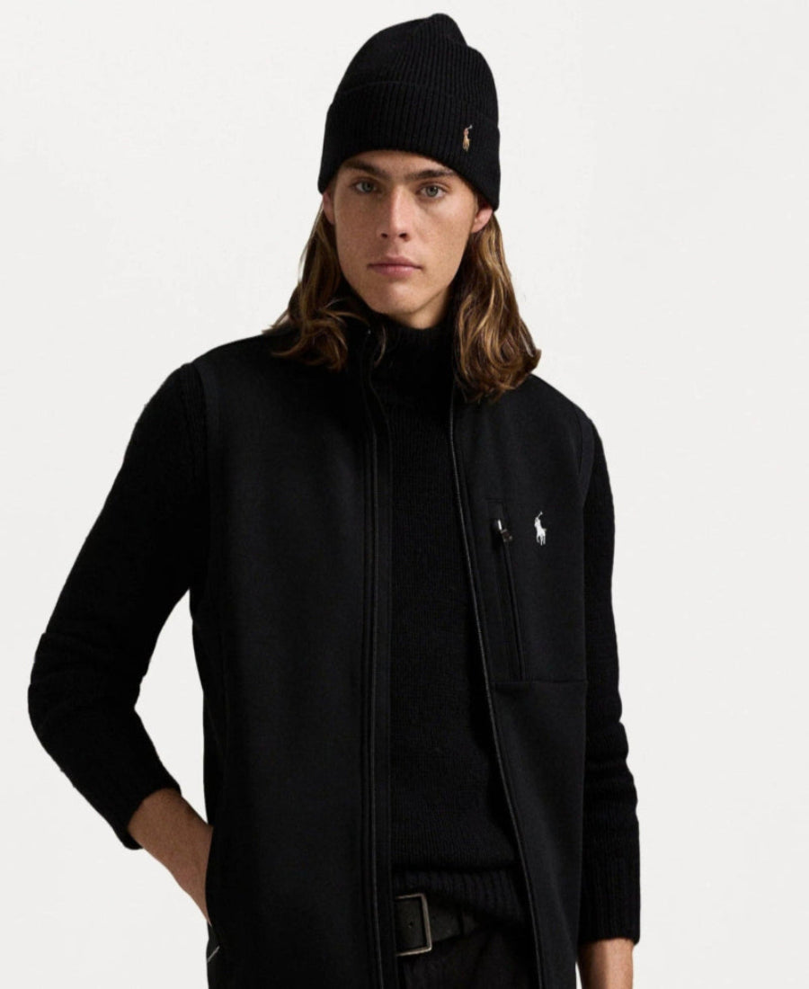 Person wearing a black jacket and beanie with a brand logo on a white background